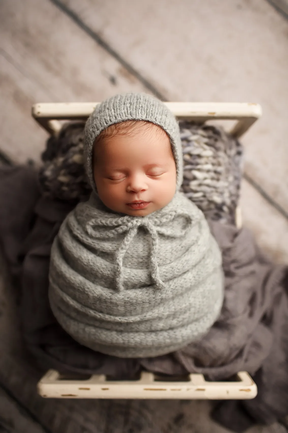 Gri örgü bonnet ve kundakla küçük ahşap yatakta uyuyan bebek