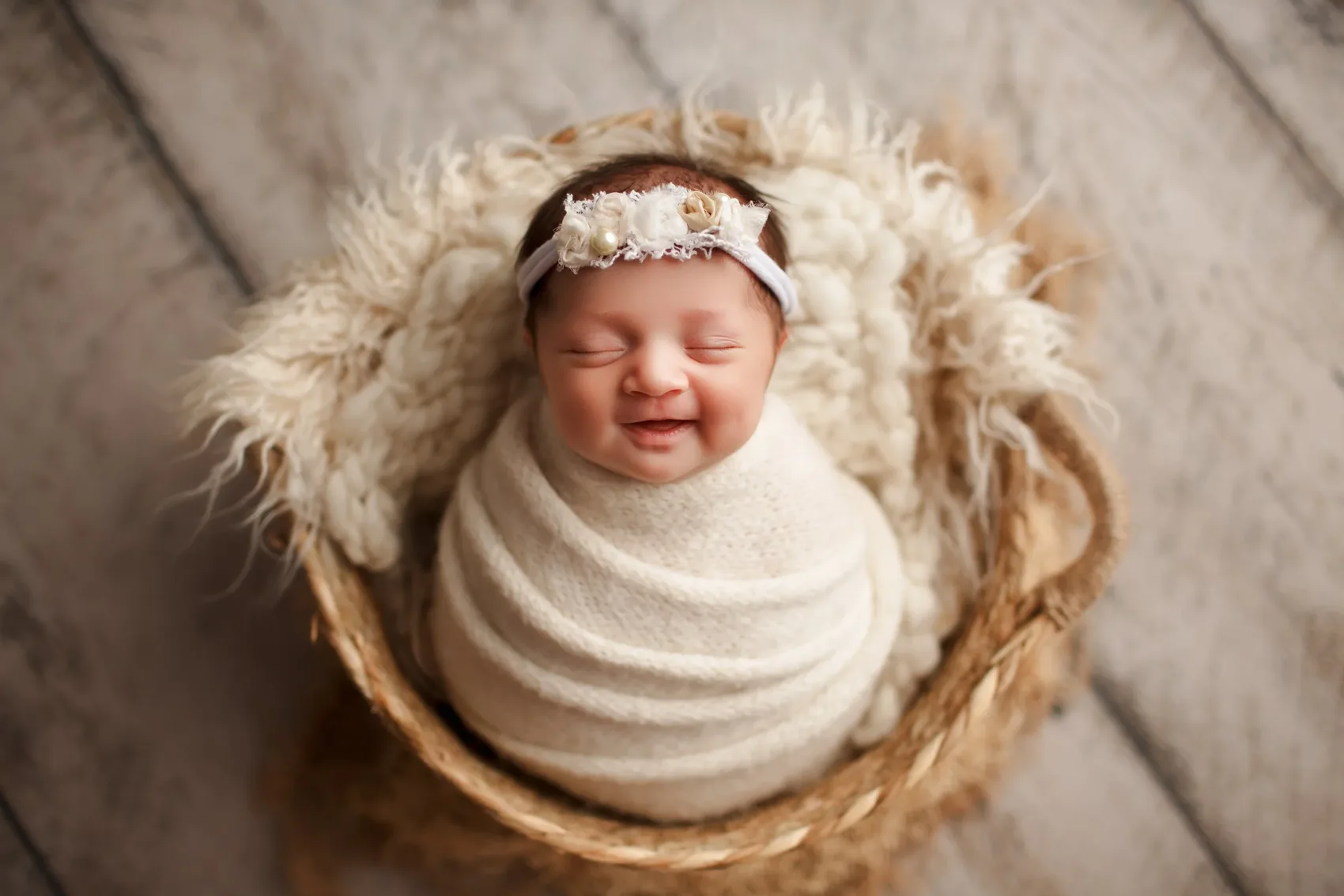 Krem kundak ve çiçekli taç ile hasır sepette gülümseyen bebek